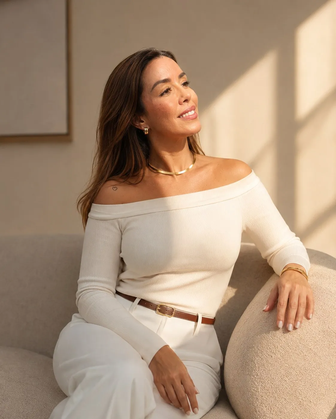 Dra. Priscilla Gil, farmacêutica esteta, sentada em um sofá claro em ambiente de luz natural