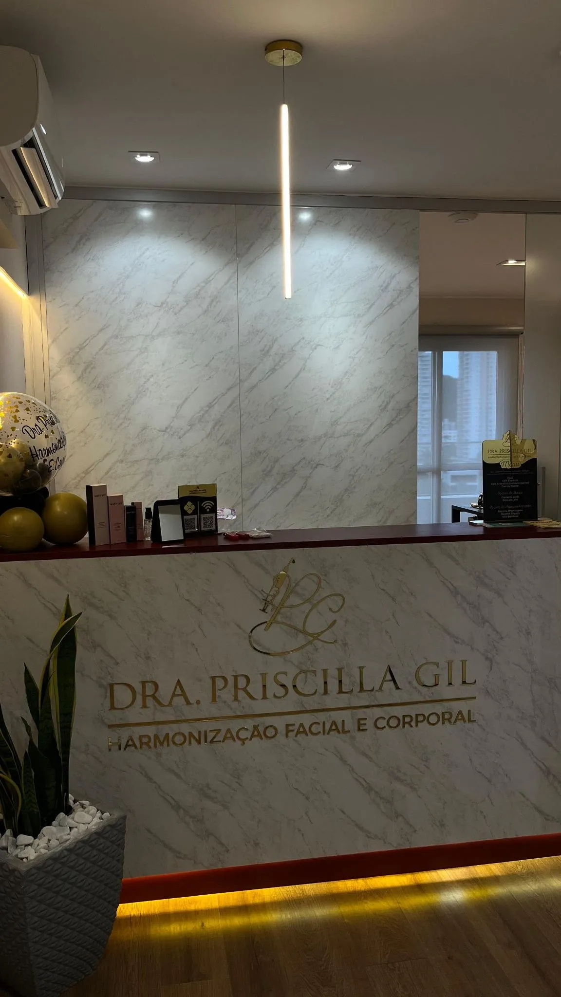 Recepção da clínica, com o logo da Dra. Priscilla Gil em parede de mármore